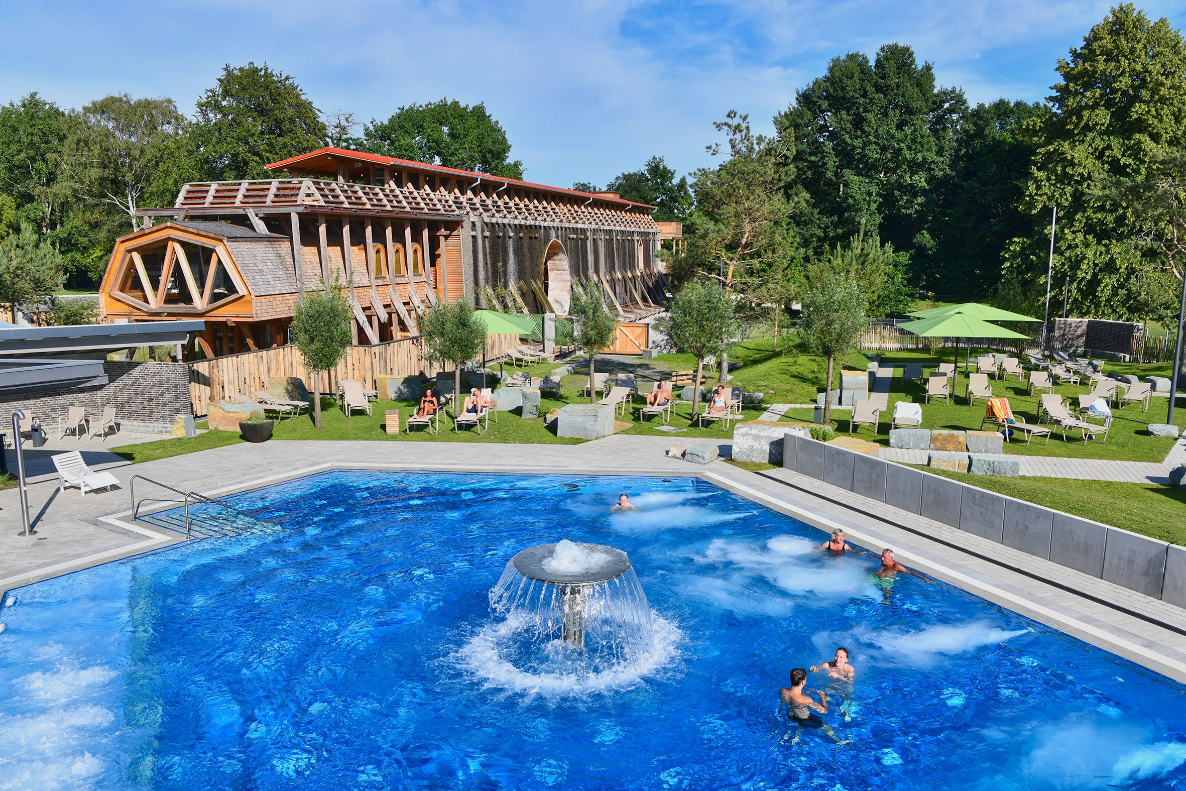 Blick auf das Außenbecken der  BördeTherme in Bad Sassendorf. Im Hintergrund steht das Gradierwerk, umgeben von Liegewiesen und entspannenden Badegästen im Sonnenschein.