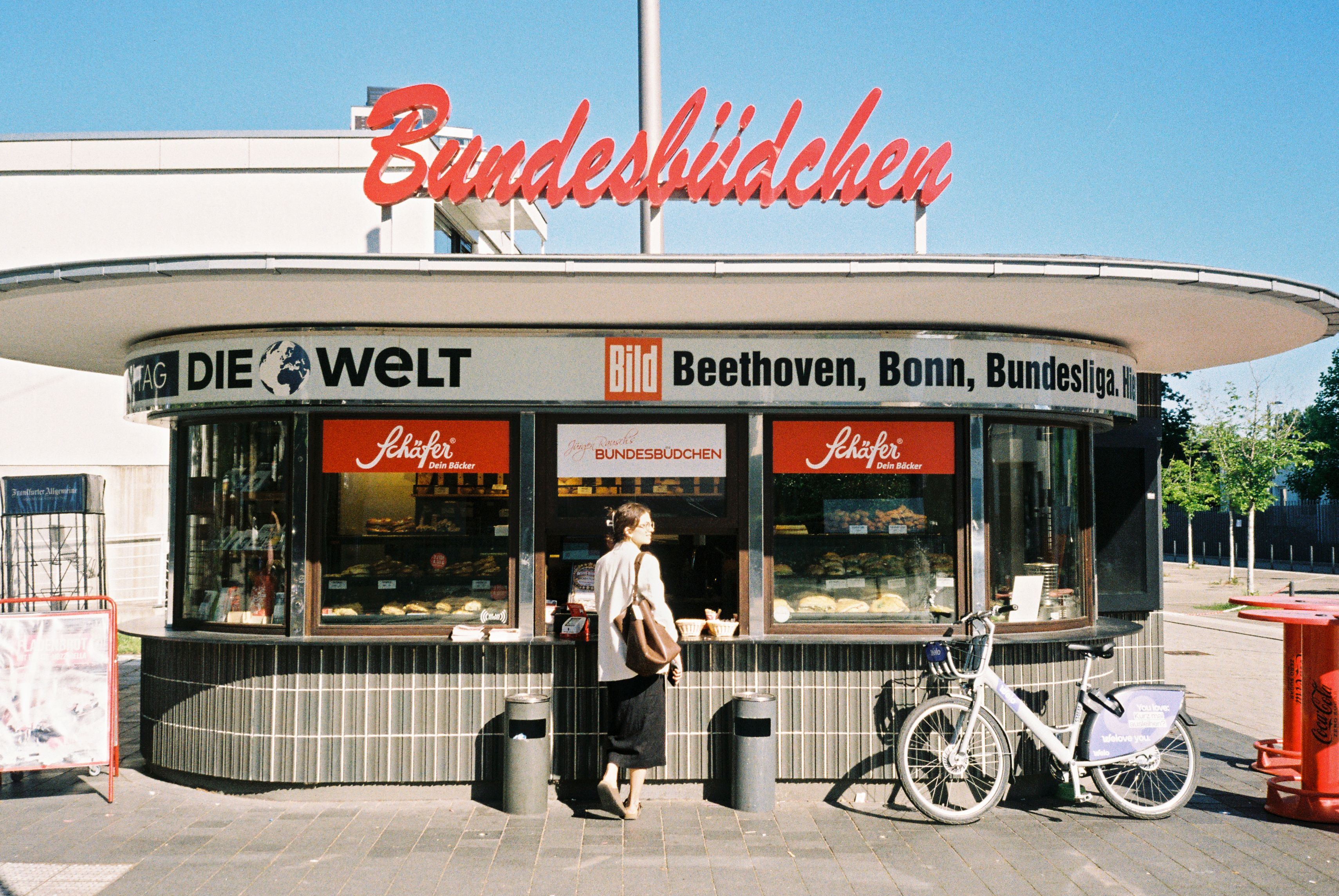 Frau steht mit abgestelltem Rent Bike am Bundesbüdchen in Bonn.