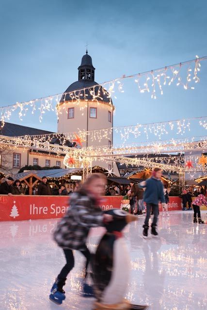 Eisläufer auf dem Siegener Weihnachtsmarkt vor dem Unteren Schloss, umgeben von festlichen Lichterketten und Ständen.