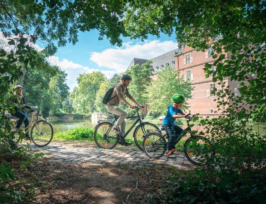 Eine Familie fährt auf einem Weg vor Schloss Bedburg entlang.