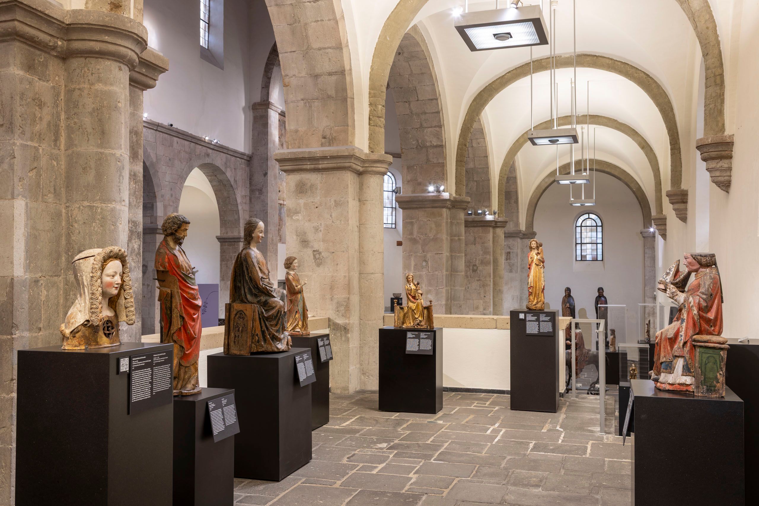 Das Museum Schnütgen in Köln zeigt mittelalterliche Skulpturen in einem historischen Kirchenraum mit hohen Gewölben und Steinbögen.