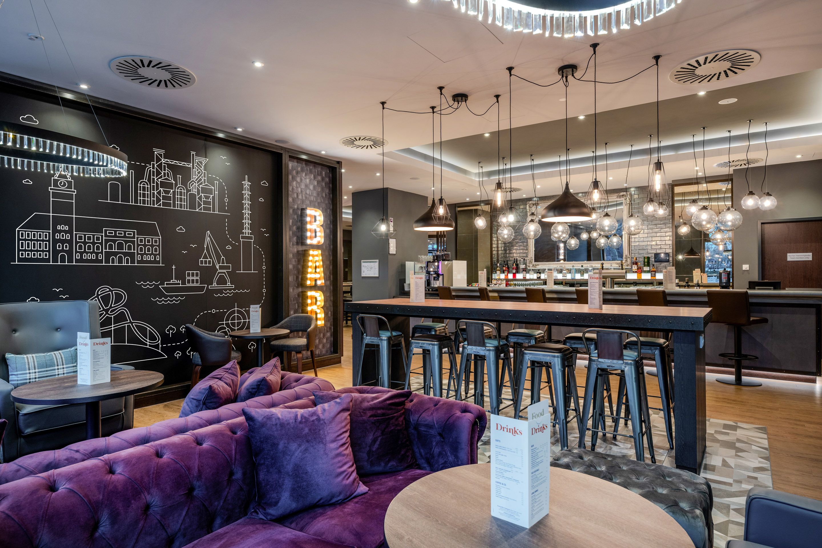 Moderne Bar mit lila Sofas, hohen Hockern und stilvollen Hängelampen.