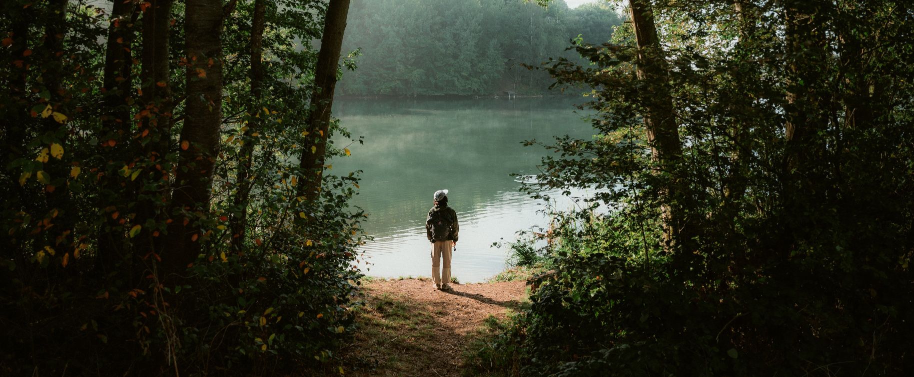 Person steht eingerahmt von Bäumen am Ufer des Freilinger Sees 