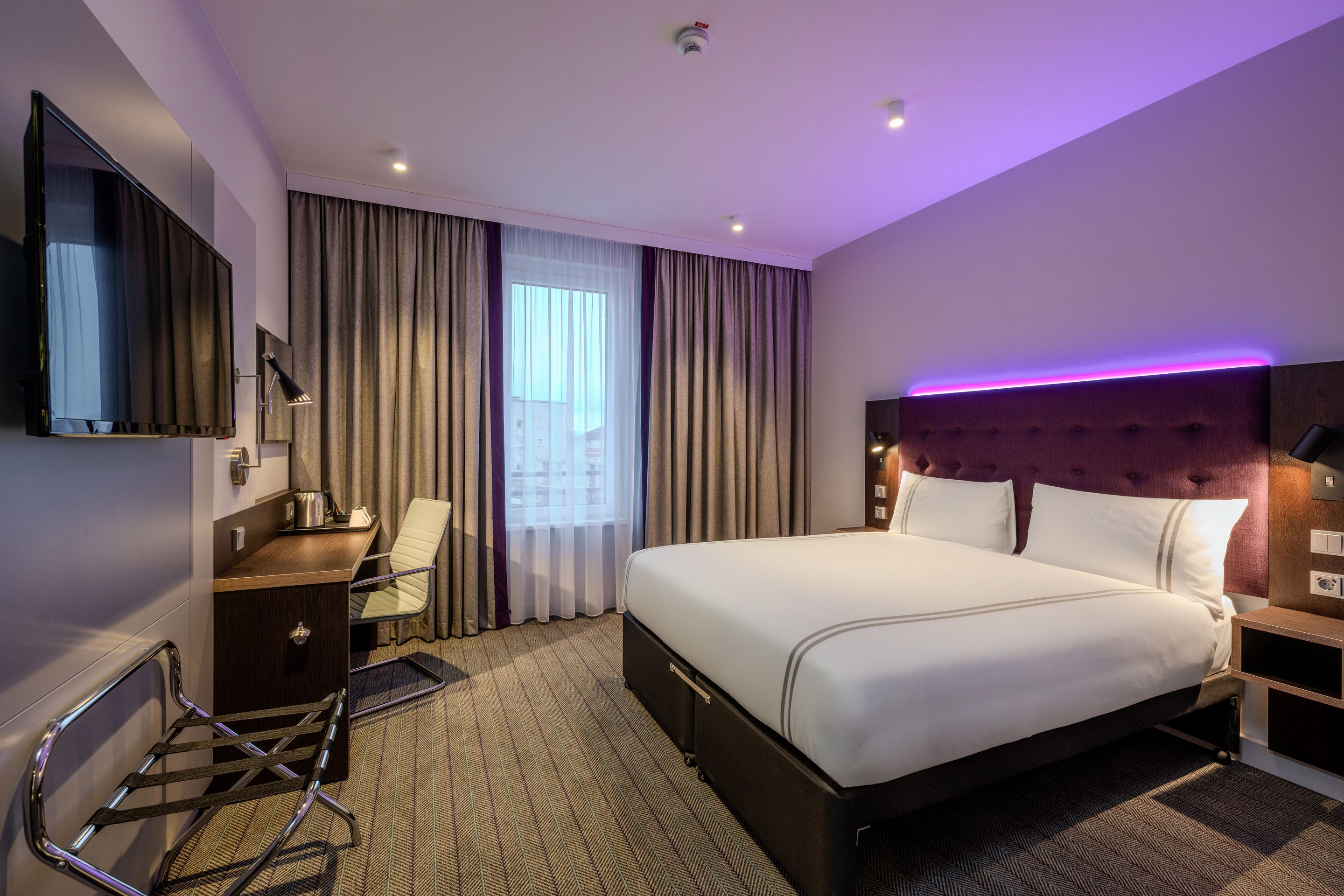 Modernes Hotelzimmer mit Doppelbett, Schreibtisch und Fernseher.