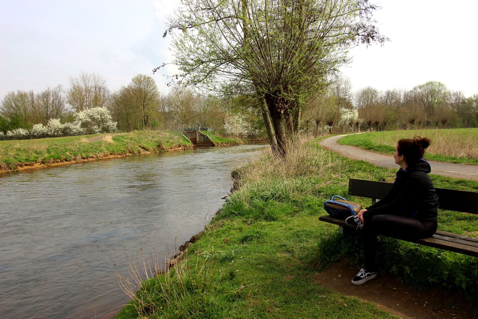 Eine Frau sitzt auf einer Bank neben dem Fluss Erft und blickt auf diesen