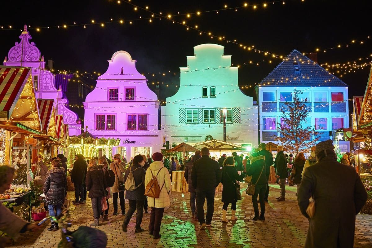 Festlich beleuchteter Nikolausmarkt in Burgsteinfurt bei Nacht. Menschen schlendern zwischen Ständen, bunte Lichter erhellen Gebäude und sorgen für eine festliche Stimmung.
