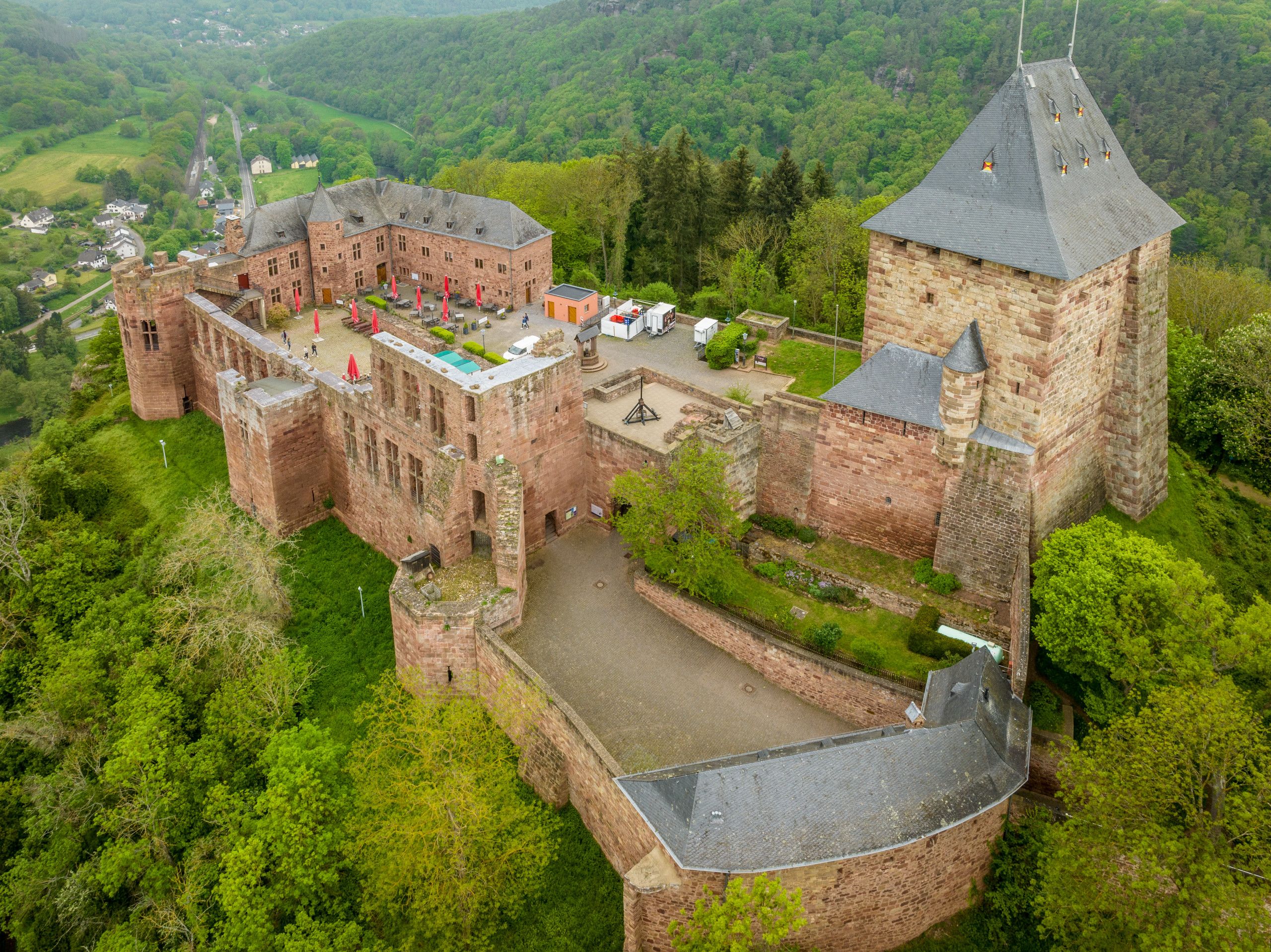 Luftaufnahme der Burg Nideggen mit roten Sandsteinmauern und Türmen, umgeben von grüner Landschaft.