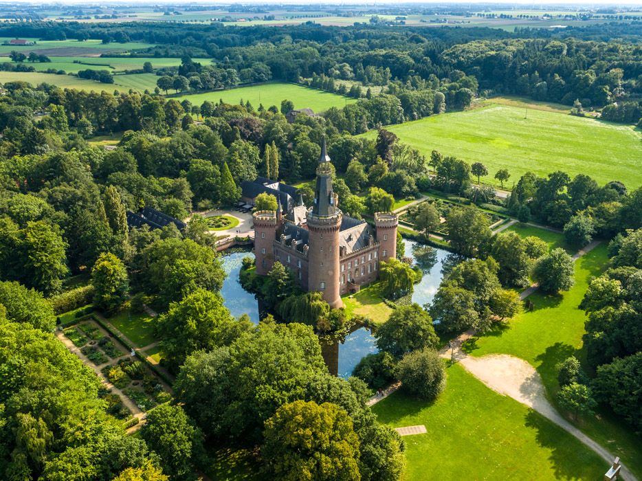 Schloss mit Wassergraben in Landschaft mit grünen Wiesen und Bäumen
