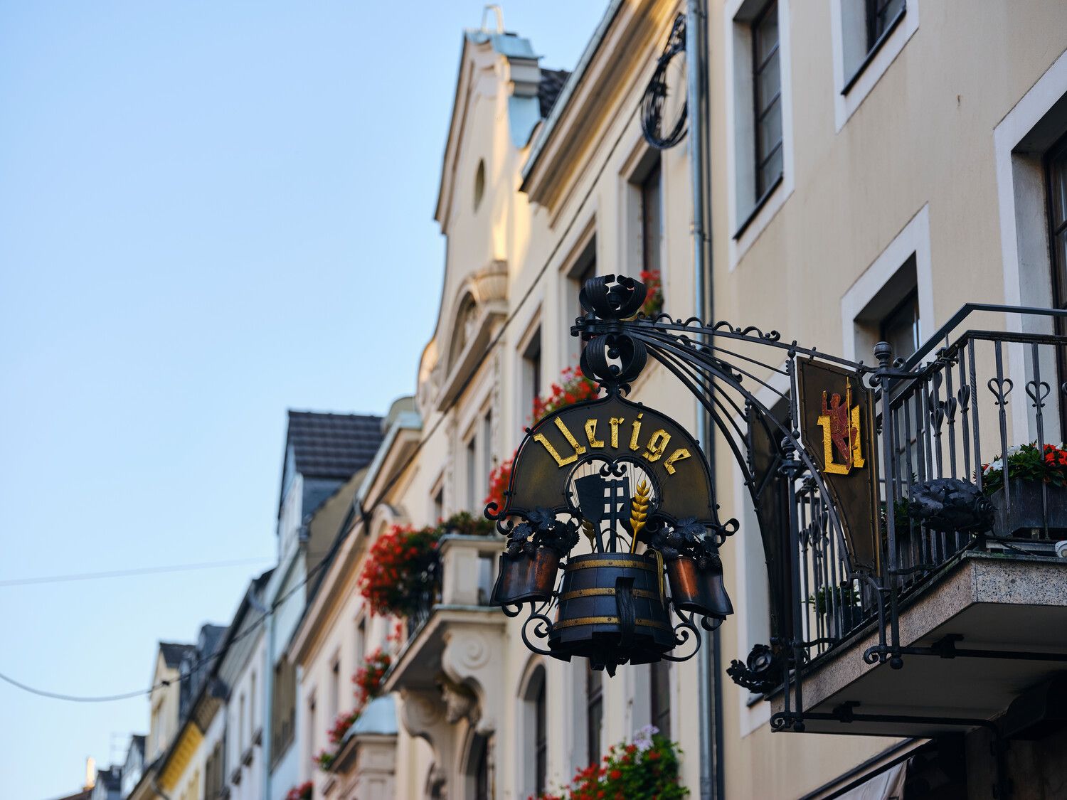 Ein traditionelles Wirtshausschild mit der Aufschrift "Uerige" hängt an einem Gebäude in einer Altstadtstraße Düsseldorfs.