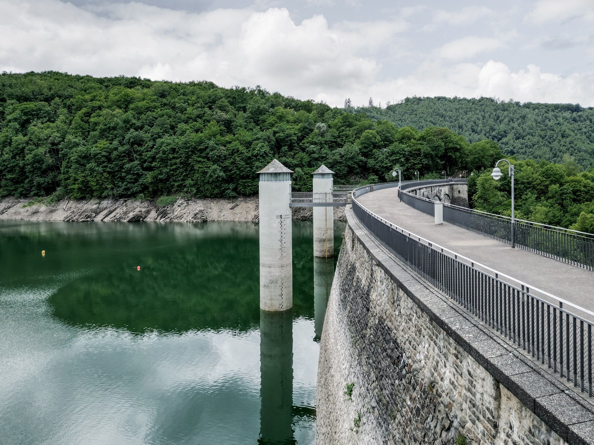Die Urfttalsperre in der Eifel zeigt eine geschwungene Staumauer, die von grünen Wäldern umgeben ist. Das Wasser reflektiert die Umgebung.