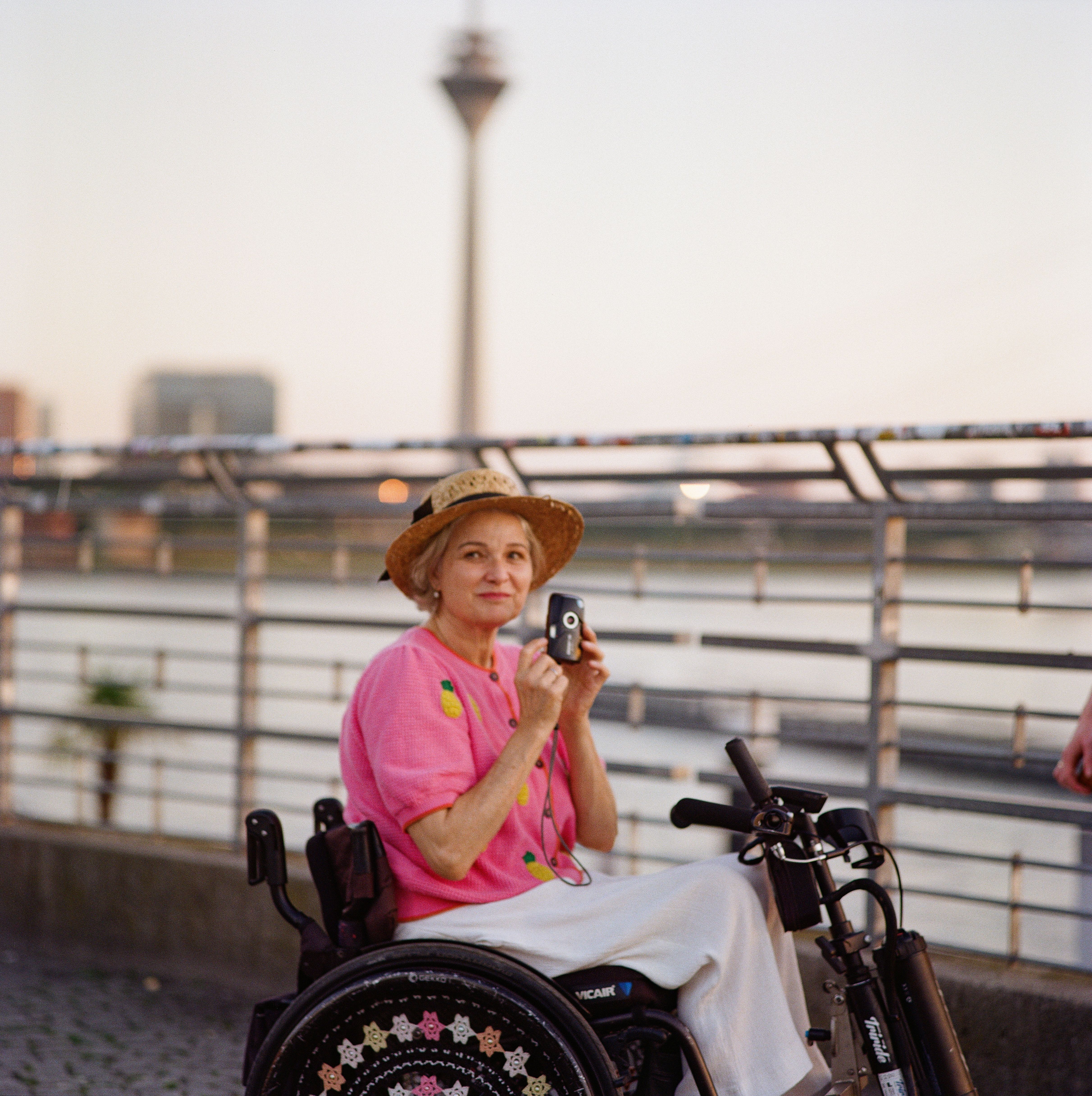 Molle & Korn, Lukasz Kus, Frau in Rollstuhl mit Kamera an der Rheinuferpromenade in Düsseldorf