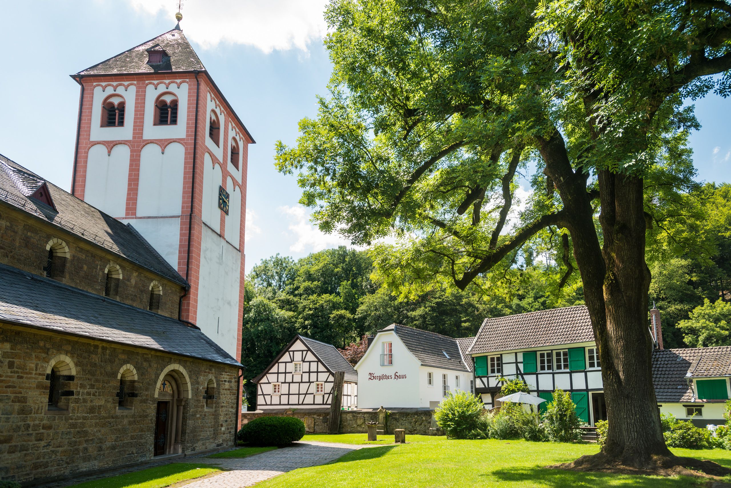 Kirche und Fachwerkhäuser in Odenthal, umgeben von Bäumen.