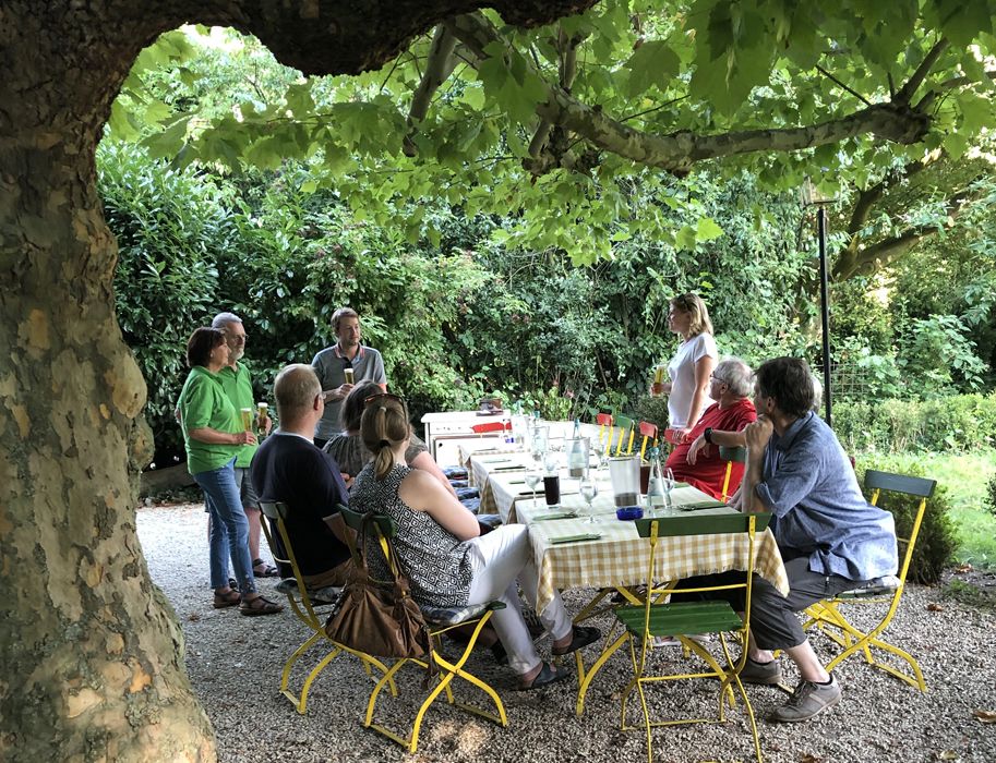 Menschen sitzen an einem Tisch im Freien unter einem Baum.