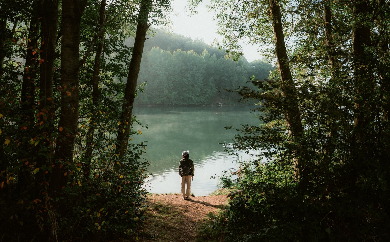 Person steht eingerahmt von Bäumen am Ufer des Freilinger Sees 