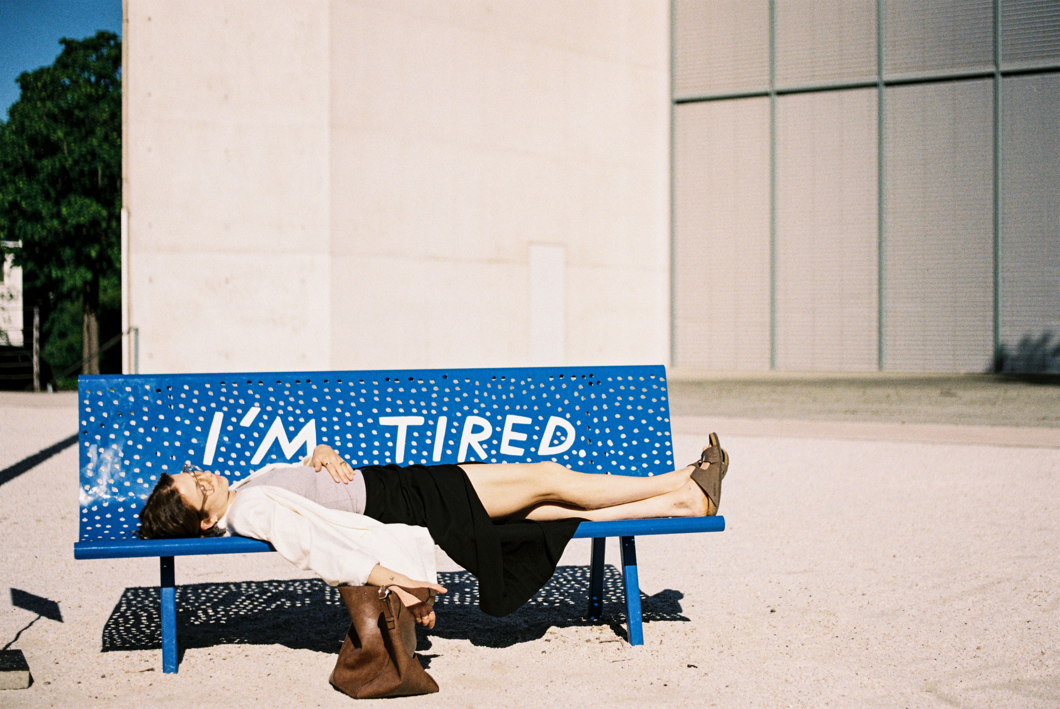 Eine Frau liegt auf einer blauen Bank mit der Aufschrift I am tired vor dem Kunstmuseum in Bonn.