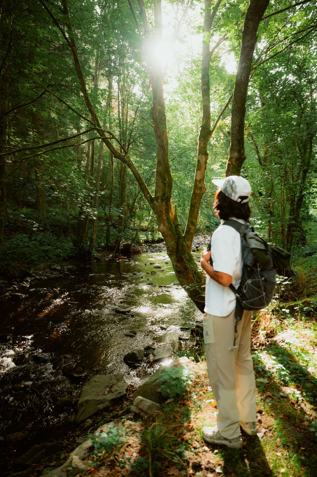 Mann steht in sonnendurchflutetem Wald am Fluss