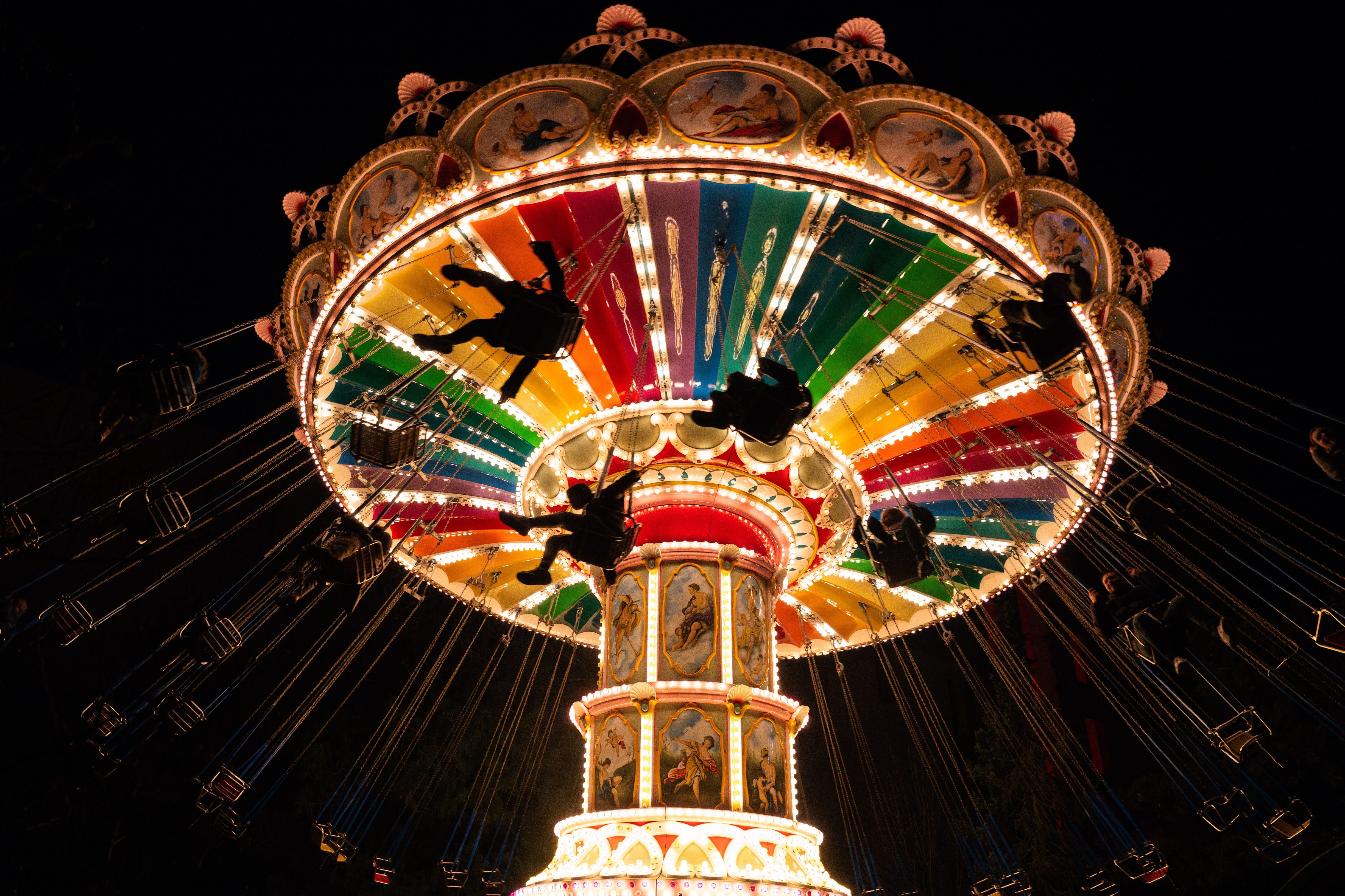 Ein beleuchtetes Kettenkarussell bei Nacht mit bunten Farben und schwebenden Silhouetten von Menschen im Wunderland Kalkar.