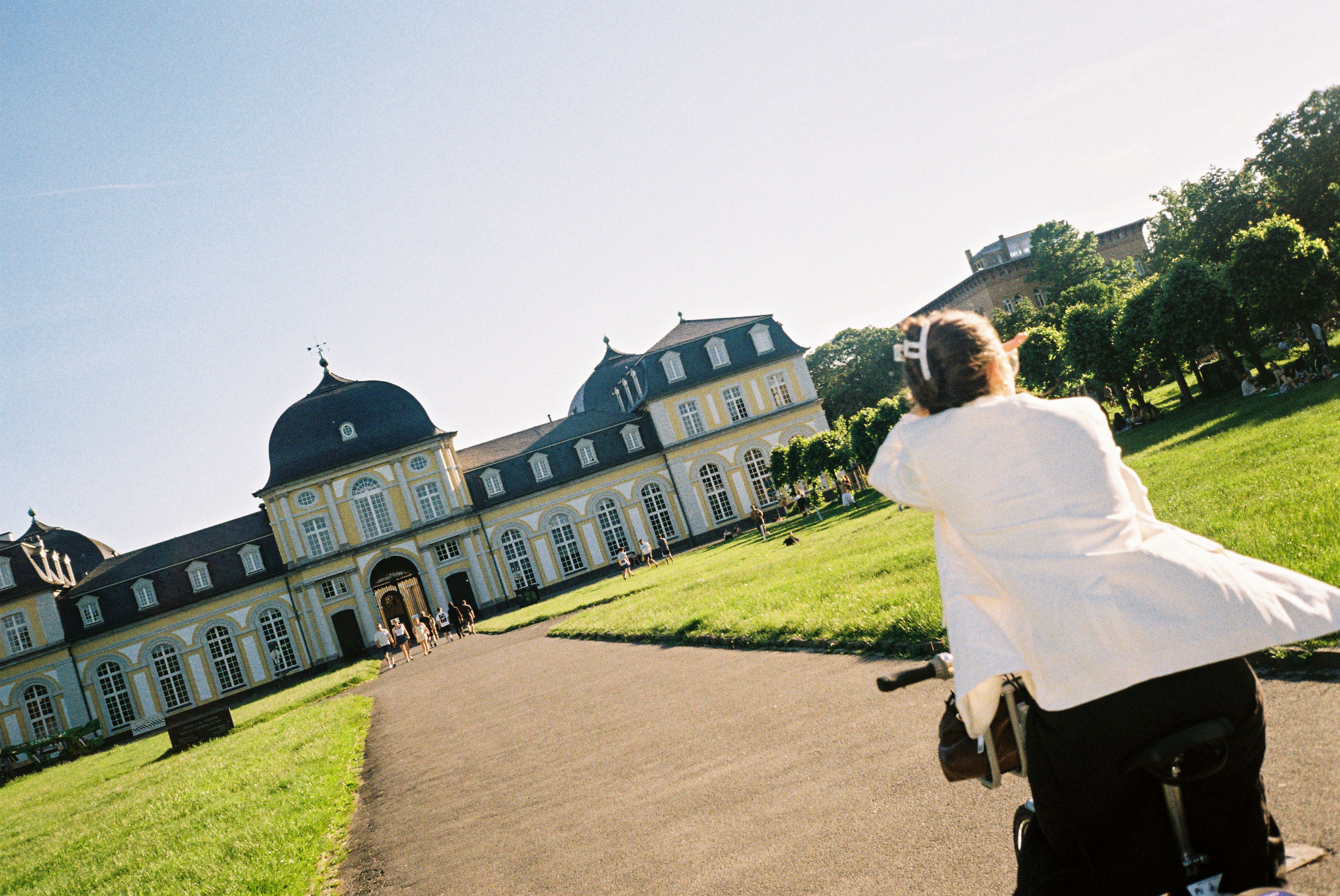 Frau auf dem Fahrrad vor dem Poppesldorfer Schloss in Bonn zwischen Wiese und Bäumen.
