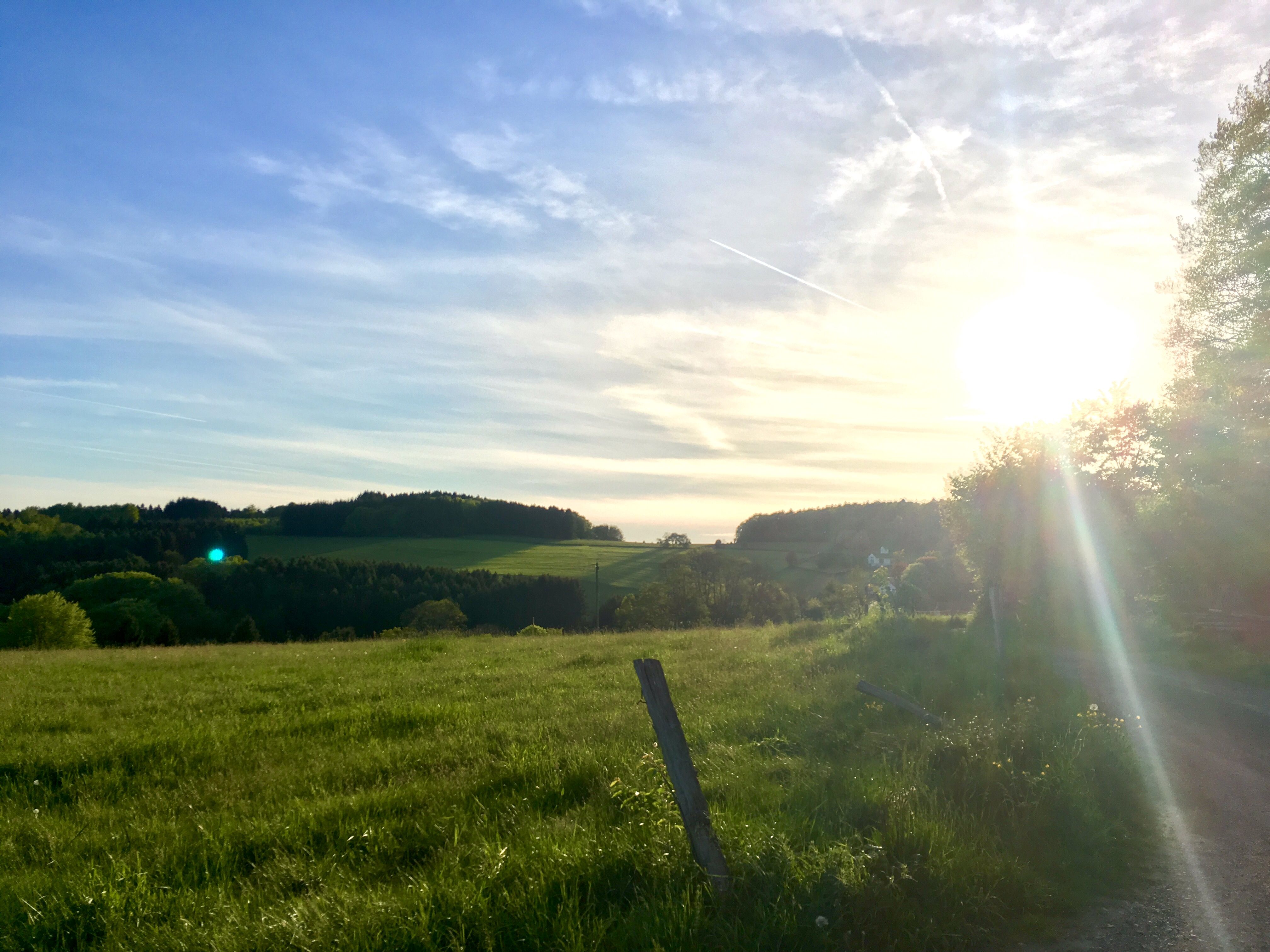 Sonnenuntergang über einer grünen Landschaft auf der Panorama-Route im Bergischen Land mit Hügeln und Bäumen.