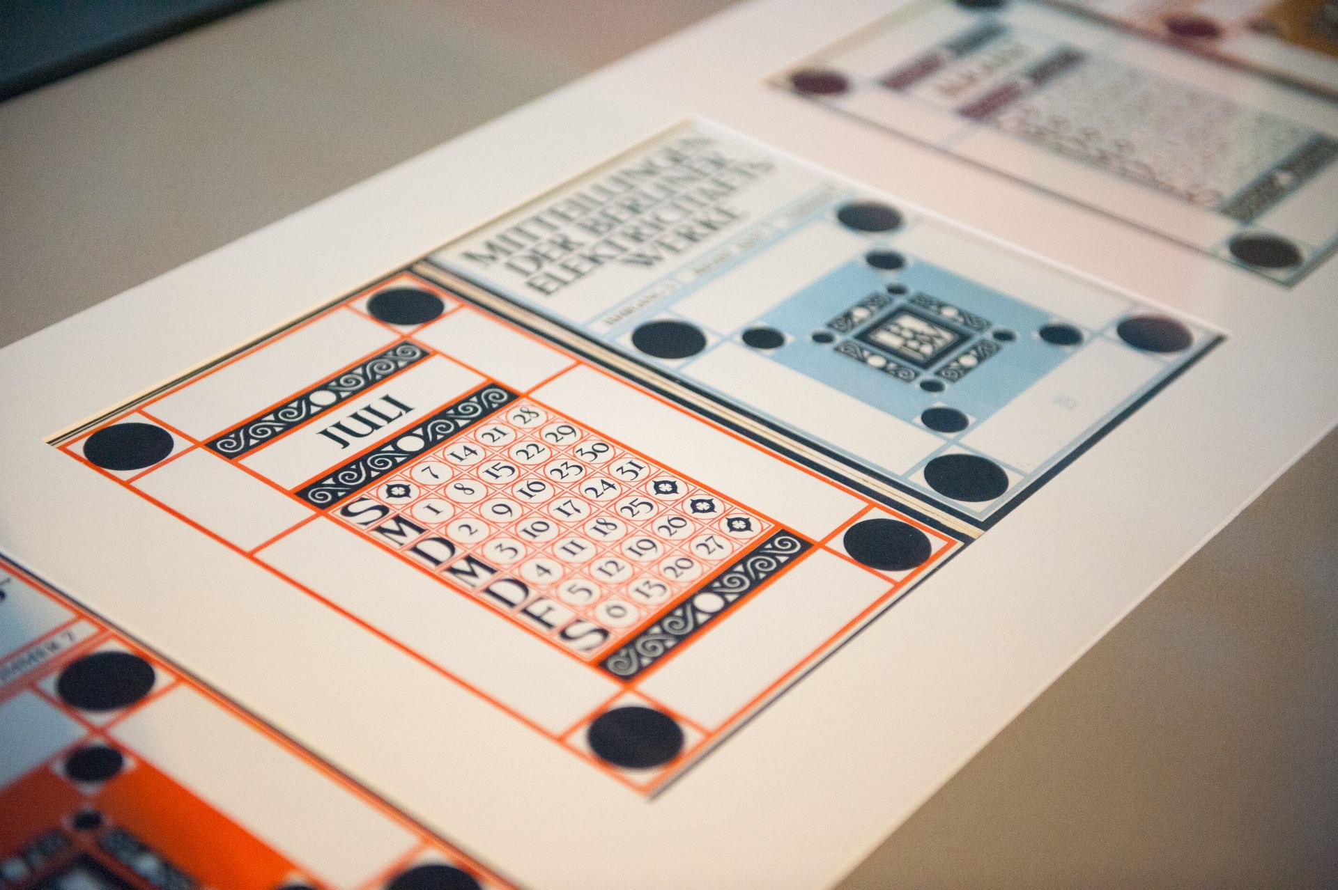 Detailaufnahme eines kunstvoll gestalteten Kalenders mit dem Monat Juli in einem Ausstellungsraum.