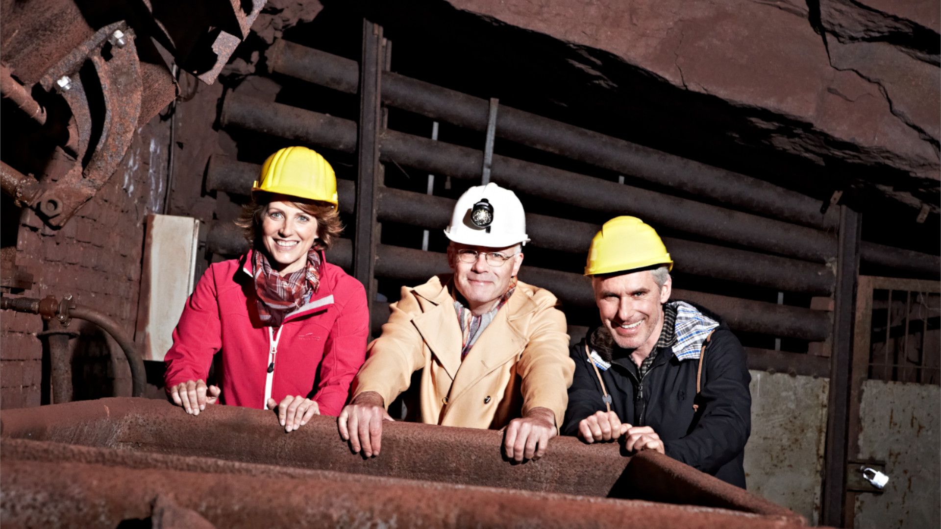Drei Besucher mit Schutzhelmen blicken in einen historischen Förderwagen.