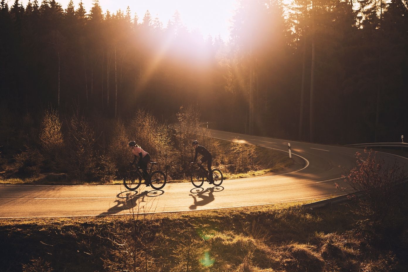 Zwei Rennradfahrer fahren im Abendlicht durch eine Kurve