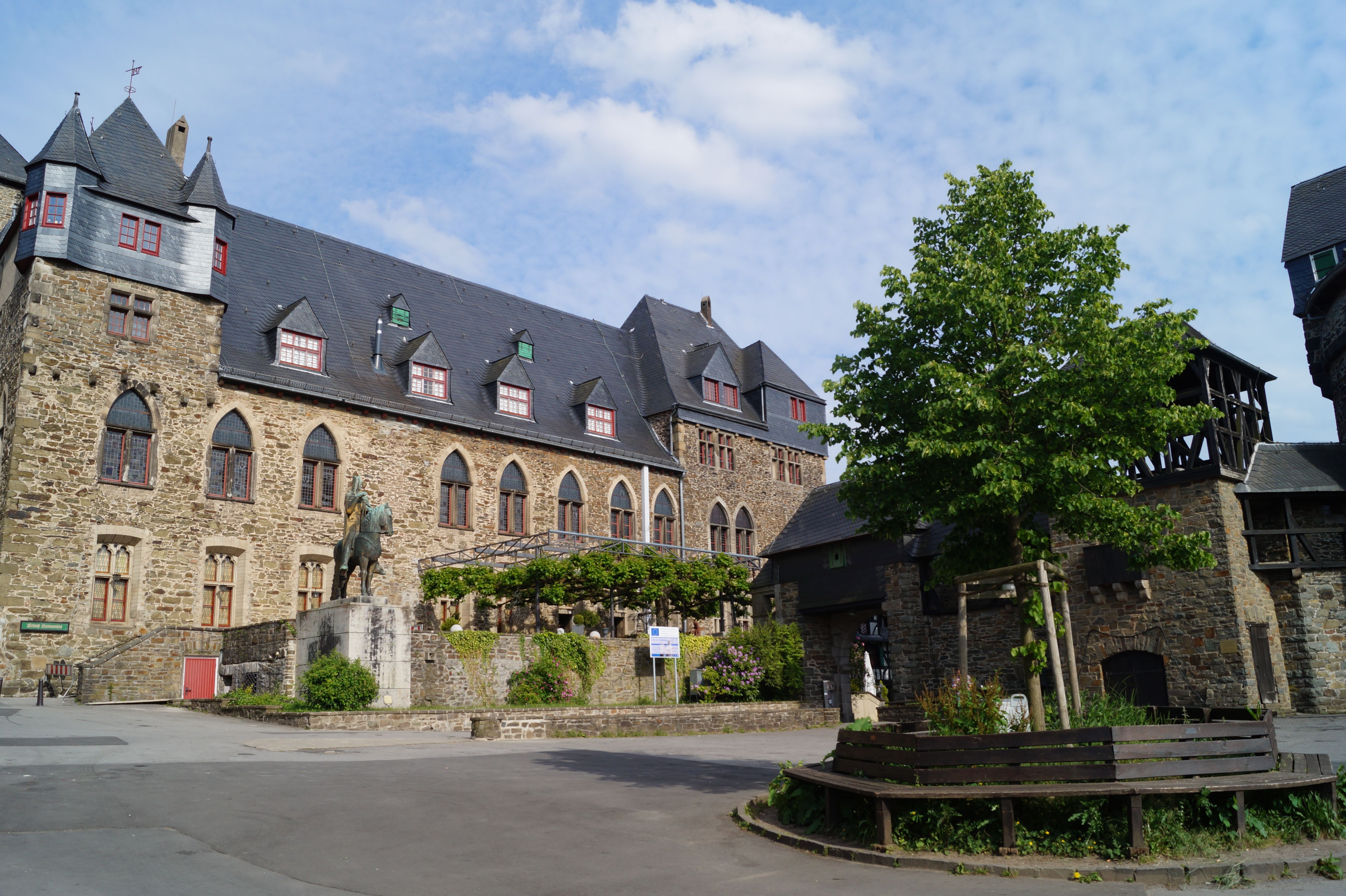 Schloss Burg mit Statue und Baum im Vordergrund.