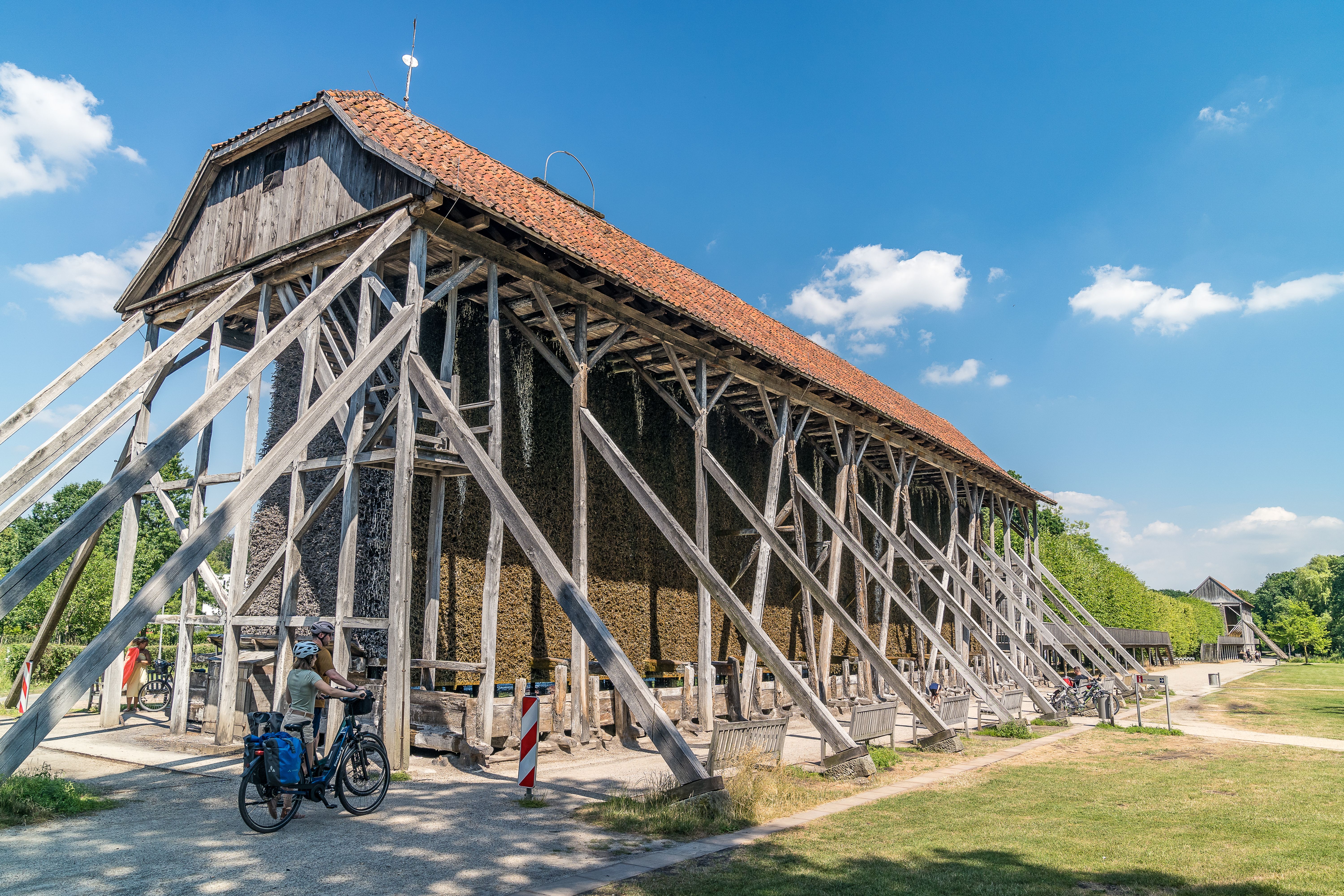 Zwischen den Holzbalken des Gradierwerks genießen Radreisende die besondere Atmosphäre der Saline Gottesgabe und eine erfrischende Pause.