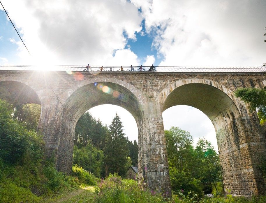 Fahrradfahrer überqueren den Vennbahn Viadukt, während die Sonne durch die Wolken scheint.