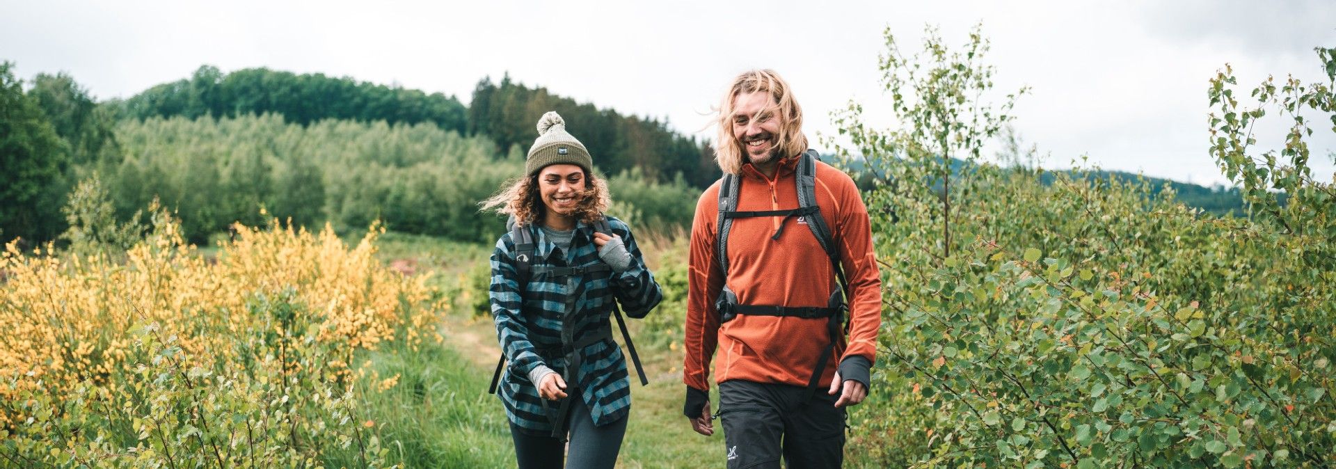 Zwei Wanderer auf einem Pfad im Grünen, umgeben von Büschen und Bäumen.