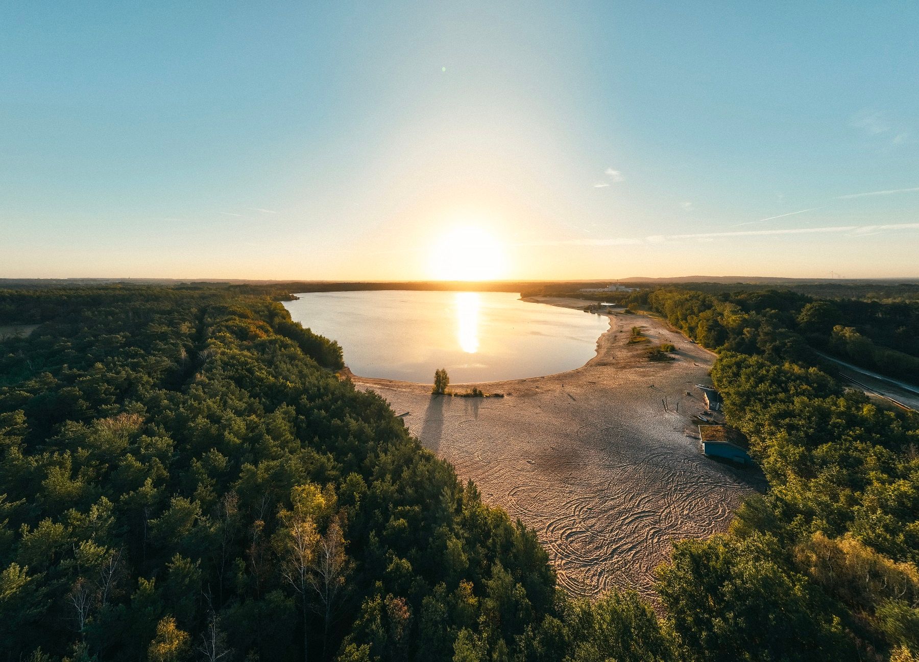 Sonnenuntergang über dem Silbersee in Haltern am See, umgeben von Wald und Sandstrand.