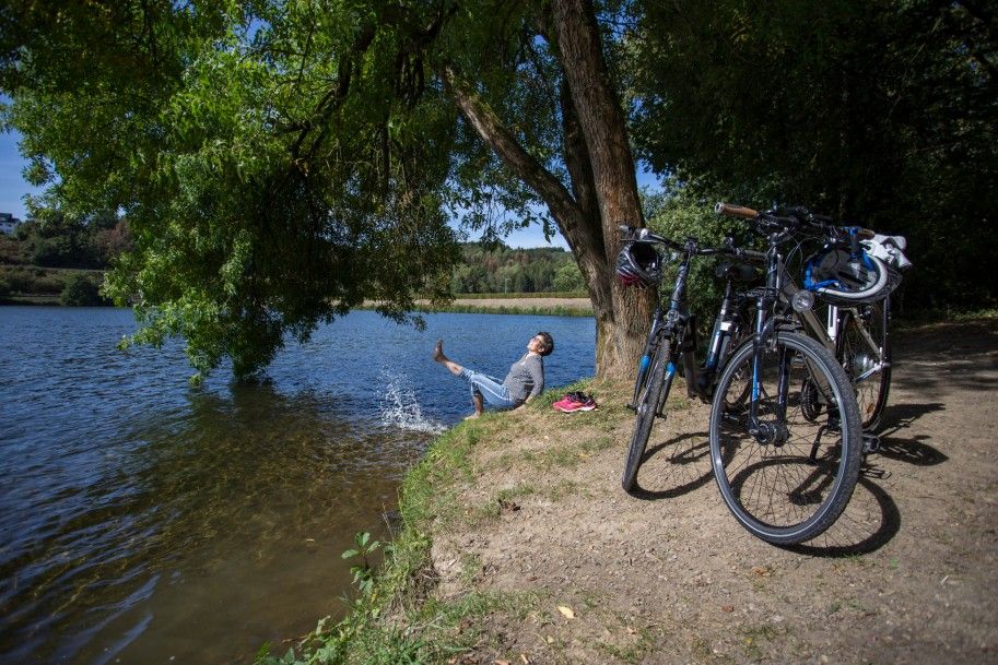 Person entspannt am Flussufer mit Fahrrädern im Vordergrund.