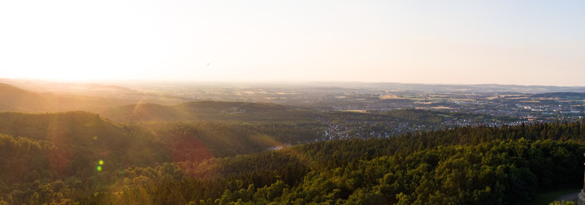 Panoramablick vom Hermannsdenkmal über bewaldete Hügel und eine weite Landschaft bei Sonnenuntergang.