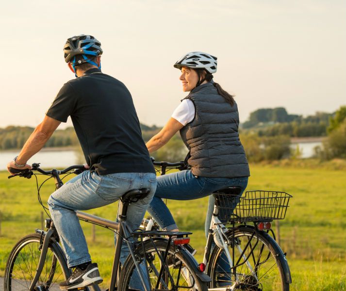 Zwei Personen mit Helmen fahren Fahrräder in einer grünen Landschaft bei Sonnenuntergang