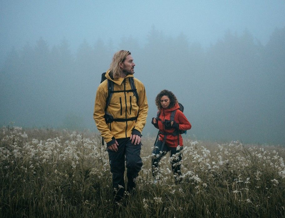 Zwei Wanderer in gelber und roter Jacke gehen durch den Nebel auf einer Wiese im Sauerland.