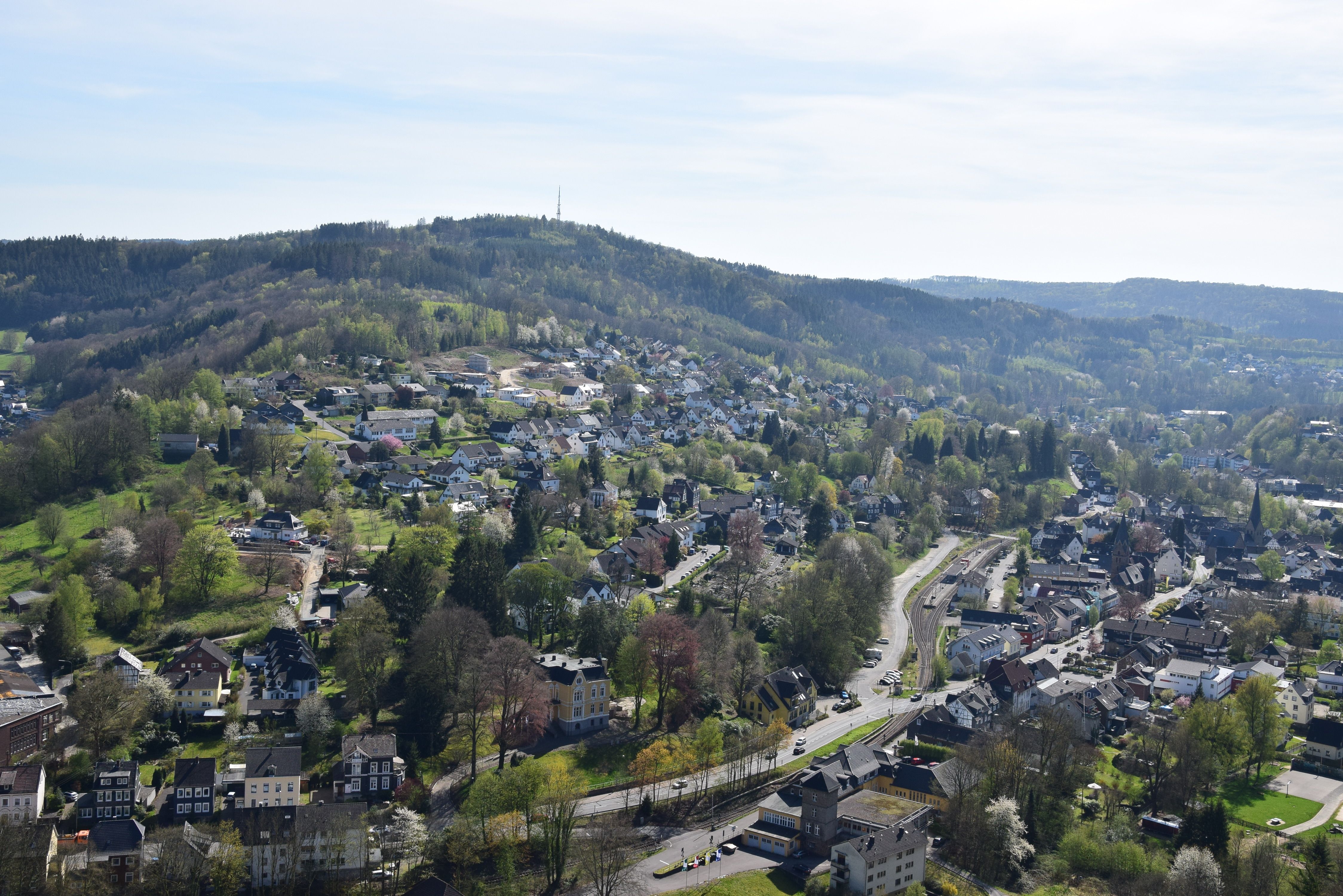 Landschaftsansicht von einem Hügel mit Häusern und Straßen, umgeben von bewaldeten Hügeln.