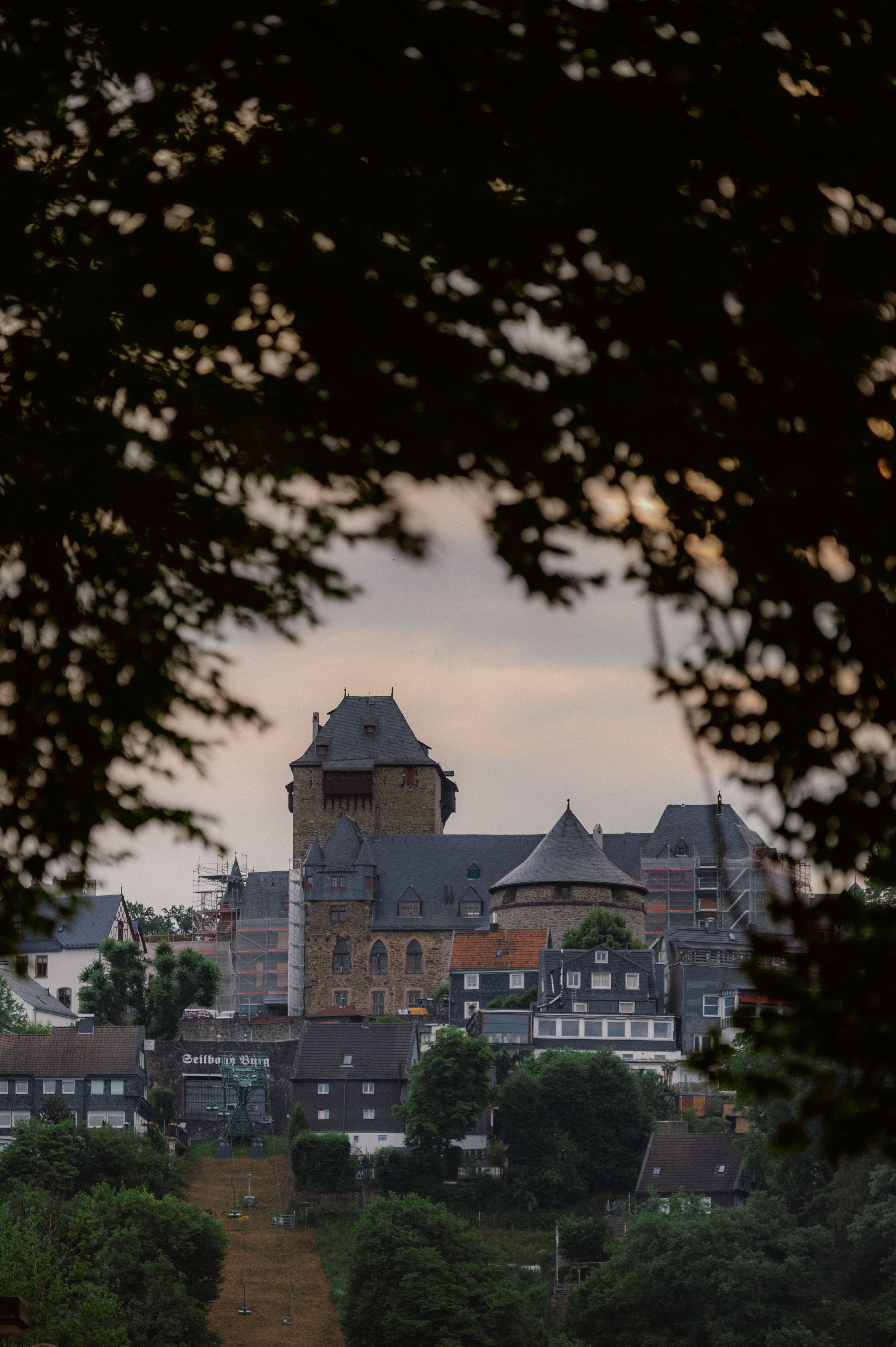 Der Bergfried von Schloss Burg ragt zwischen den Bäumen gen Himmel empor