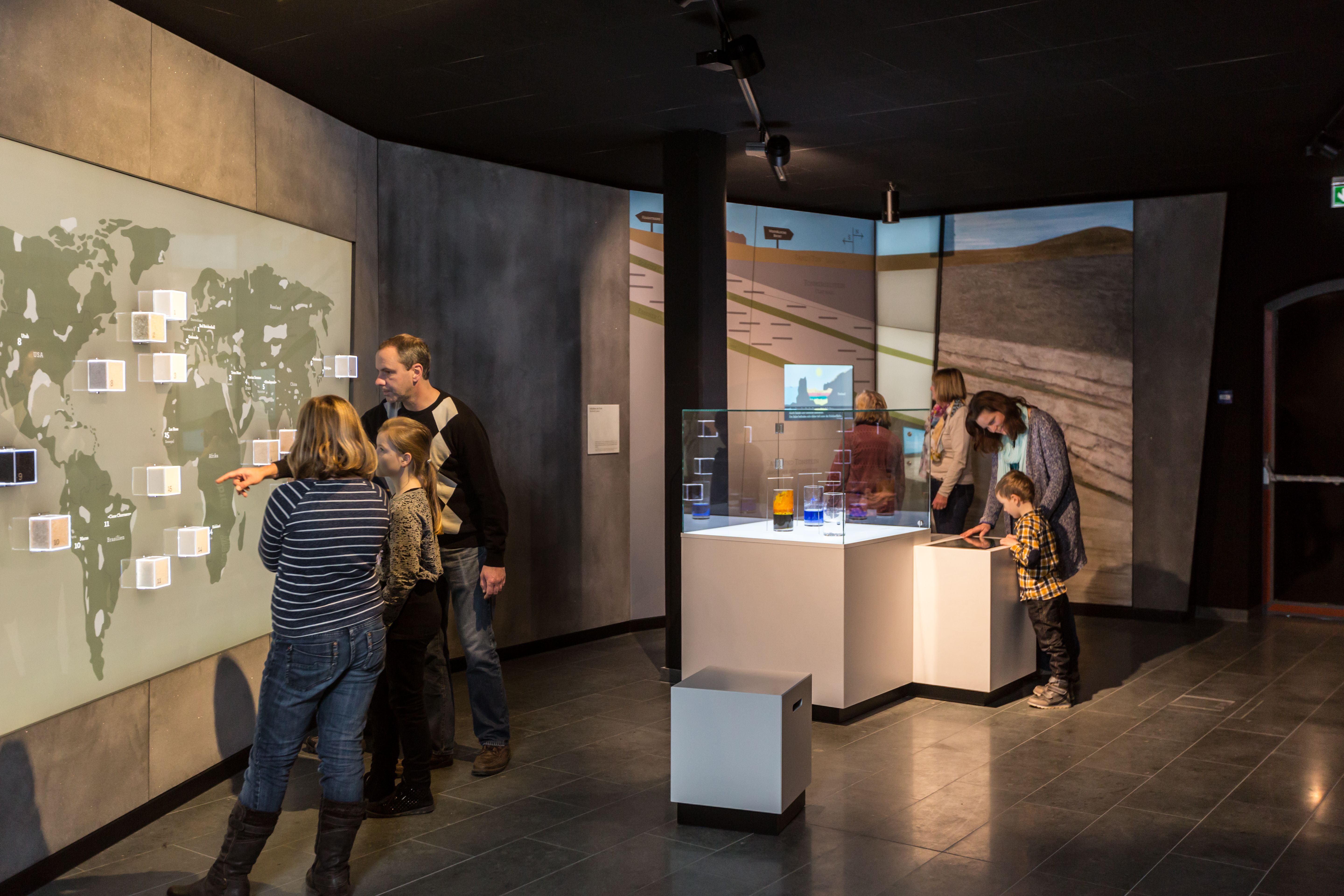 Das Bild zeigt Besucher in einer modernen Ausstellung der Westfälischen Salzwelten, die interaktive Stationen und eine große Weltkarte erkunden.