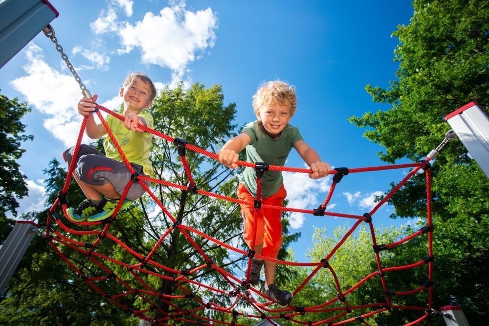 Zwei Kinder klettern fröhlich auf einem roten Kletternetz im Kurpark Brilon.