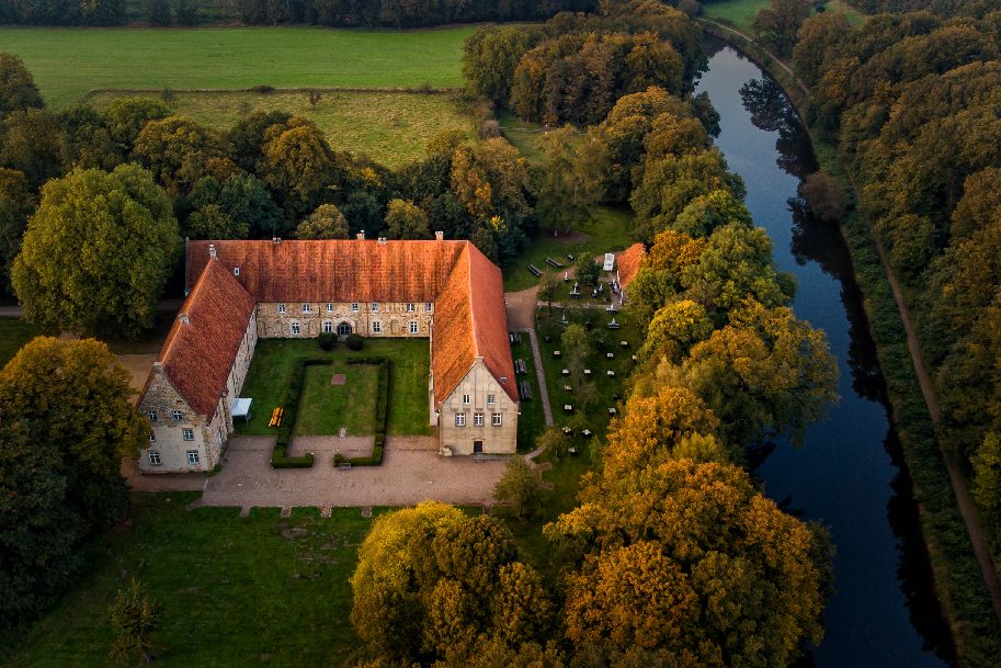 Luftaufnahme des Klosters Bentlage umgeben von Bäumen und einem Fluss.
