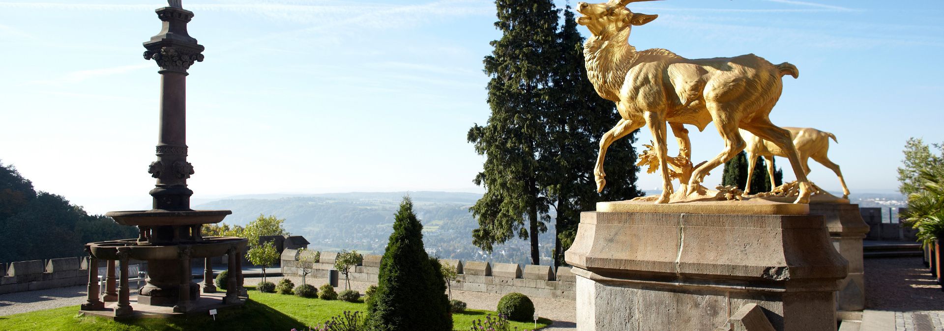 Goldene Hirschskulptur und Brunnen auf der Venusterrasse mit Landschaft im Hintergrund.