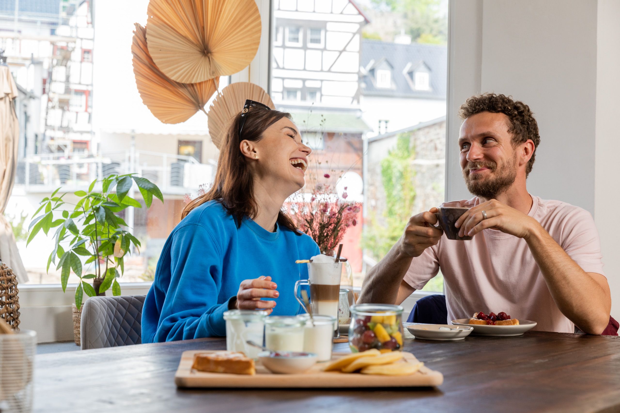 Zwei Personen sitzen am Tisch, frühstücken und lachen zusammen in einem hellen, gemütlichen Raum.