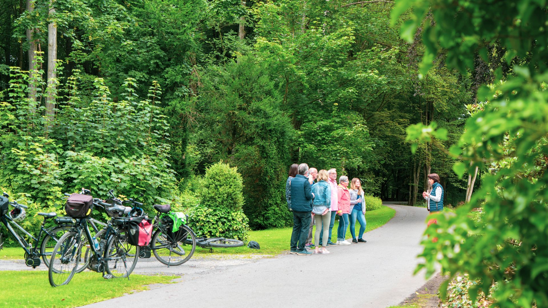 Gruppe von Menschen steht auf einem Waldweg neben Fahrrädern.