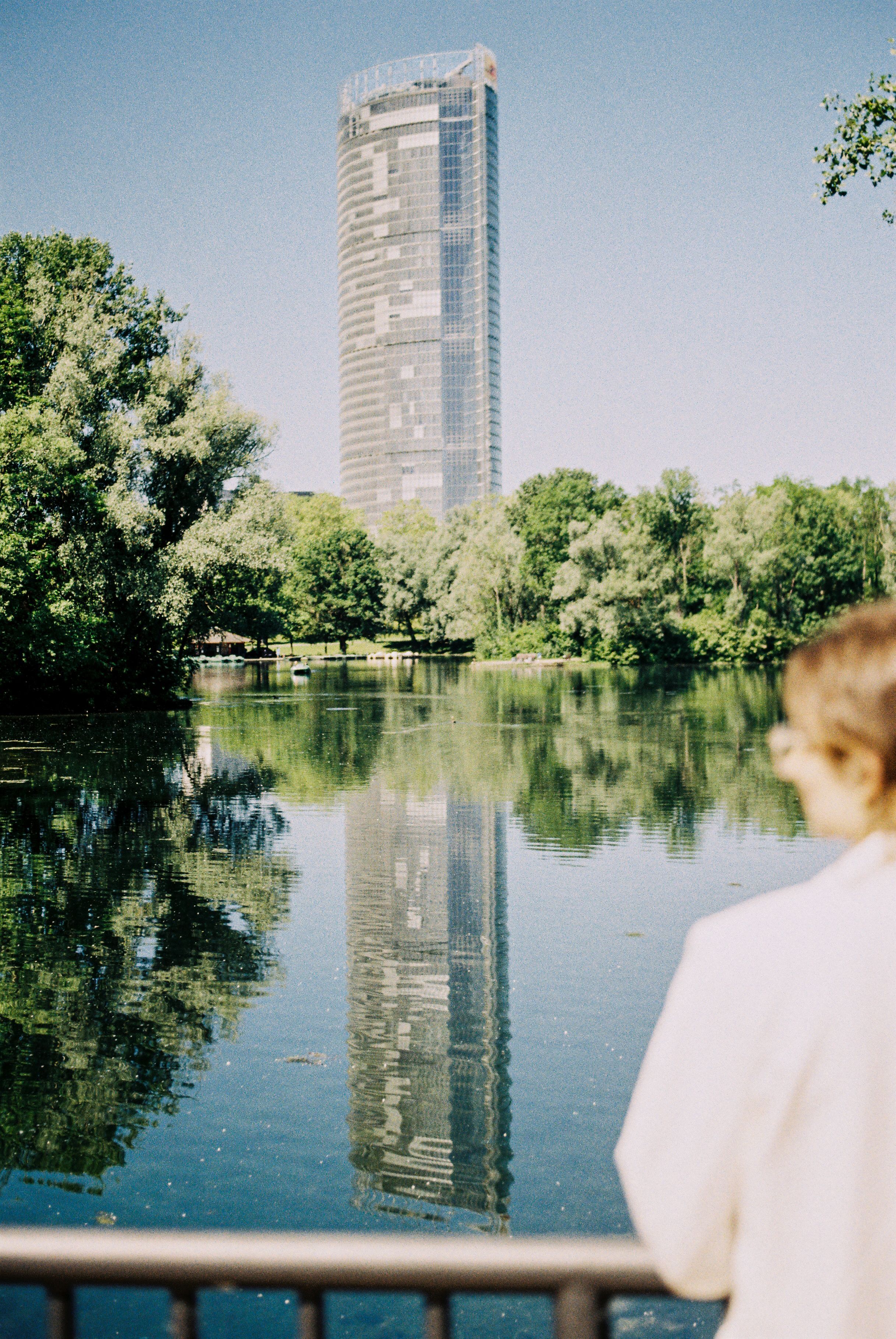 Frau steht am Rheinauensee mit Blick auf Bäume und den Post Tower in Bonn.