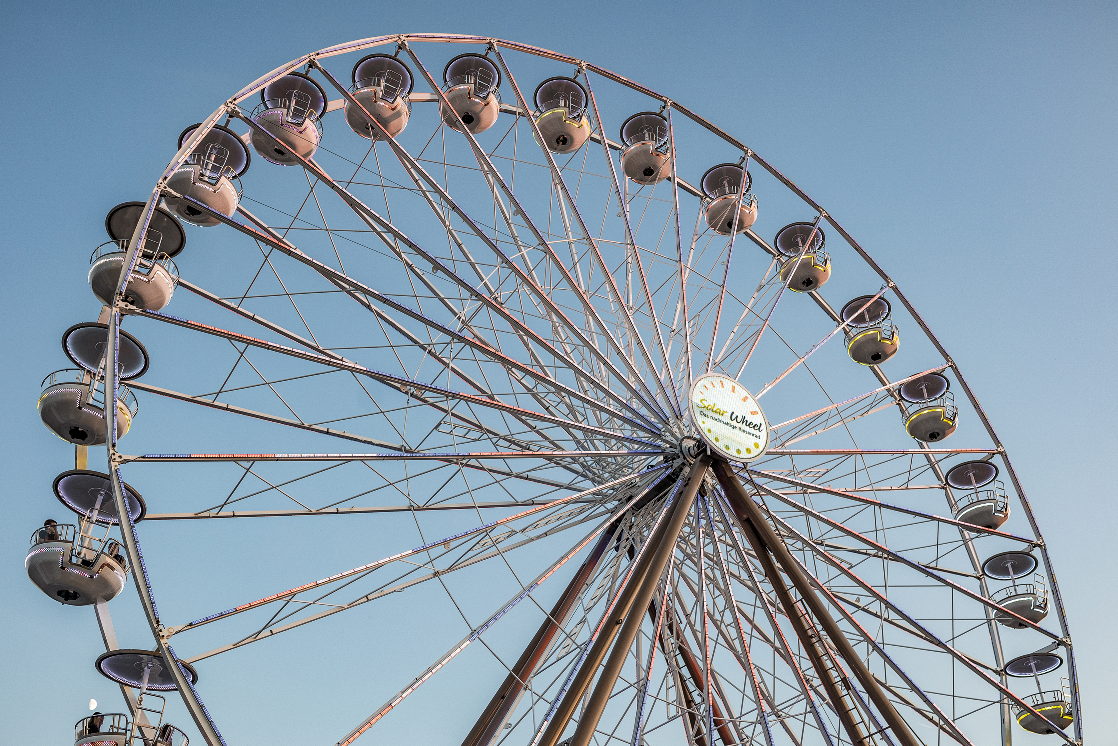 Riesenrad „Solar Wheel“ mit beleuchteten Gondeln vor blauem Himmel, von unten fotografiert.