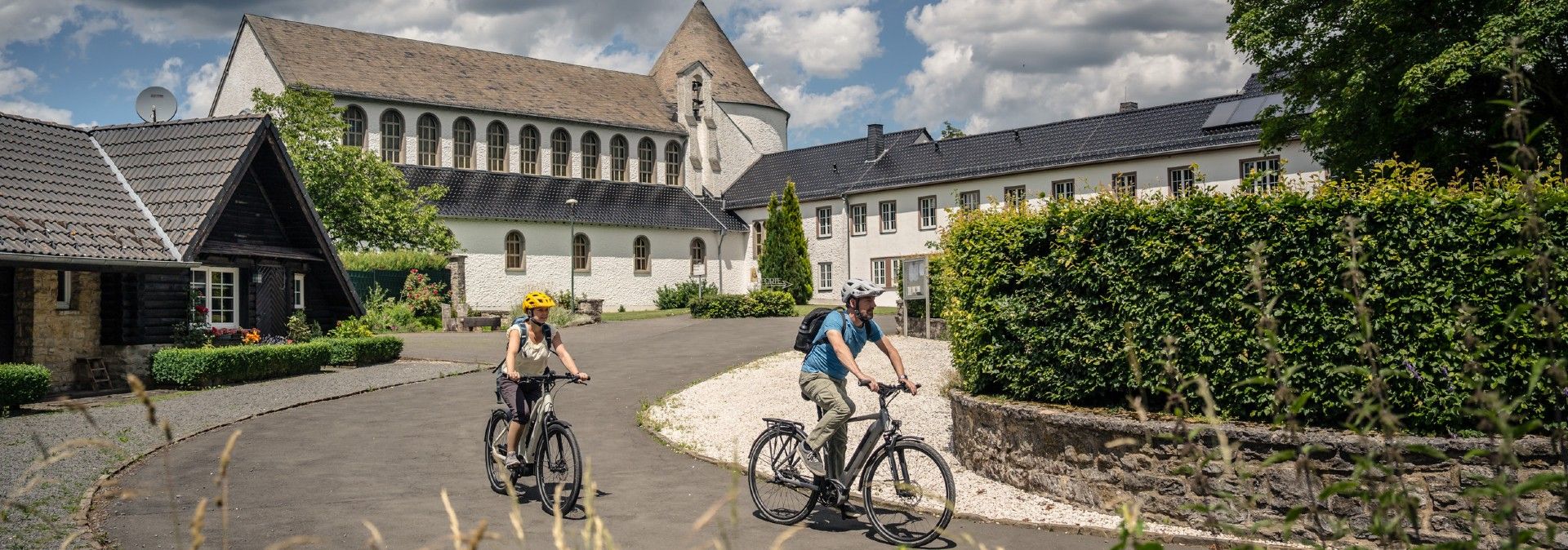 Zwei Radfahrer auf einer Straße vor einem historischen Gebäude mit Turm.