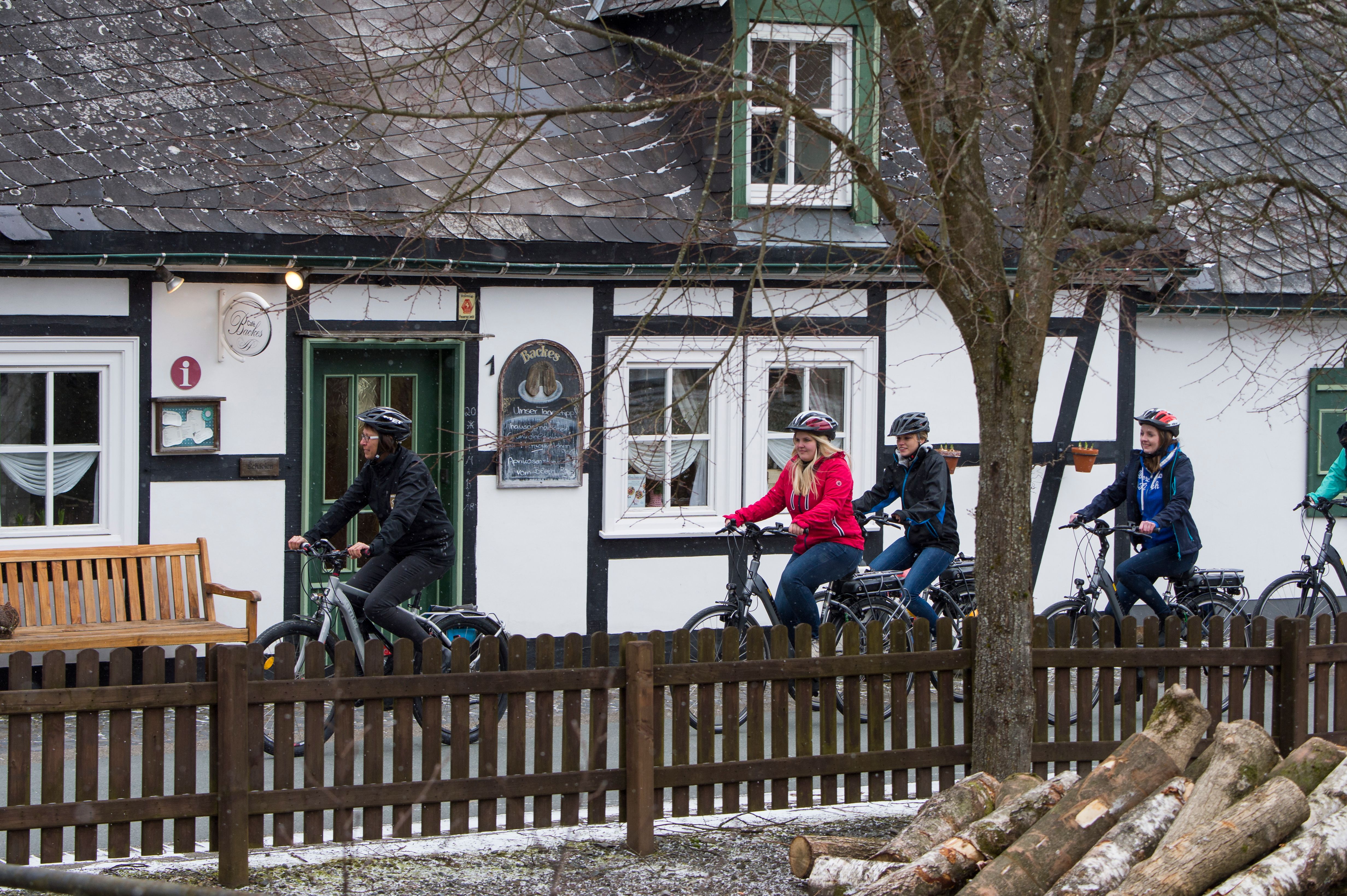 Gruppe von Radfahrern auf E-Bikes vor einem Fachwerkhaus im Sauerland. Es ist winterlich, mit leichtem Schneefall.