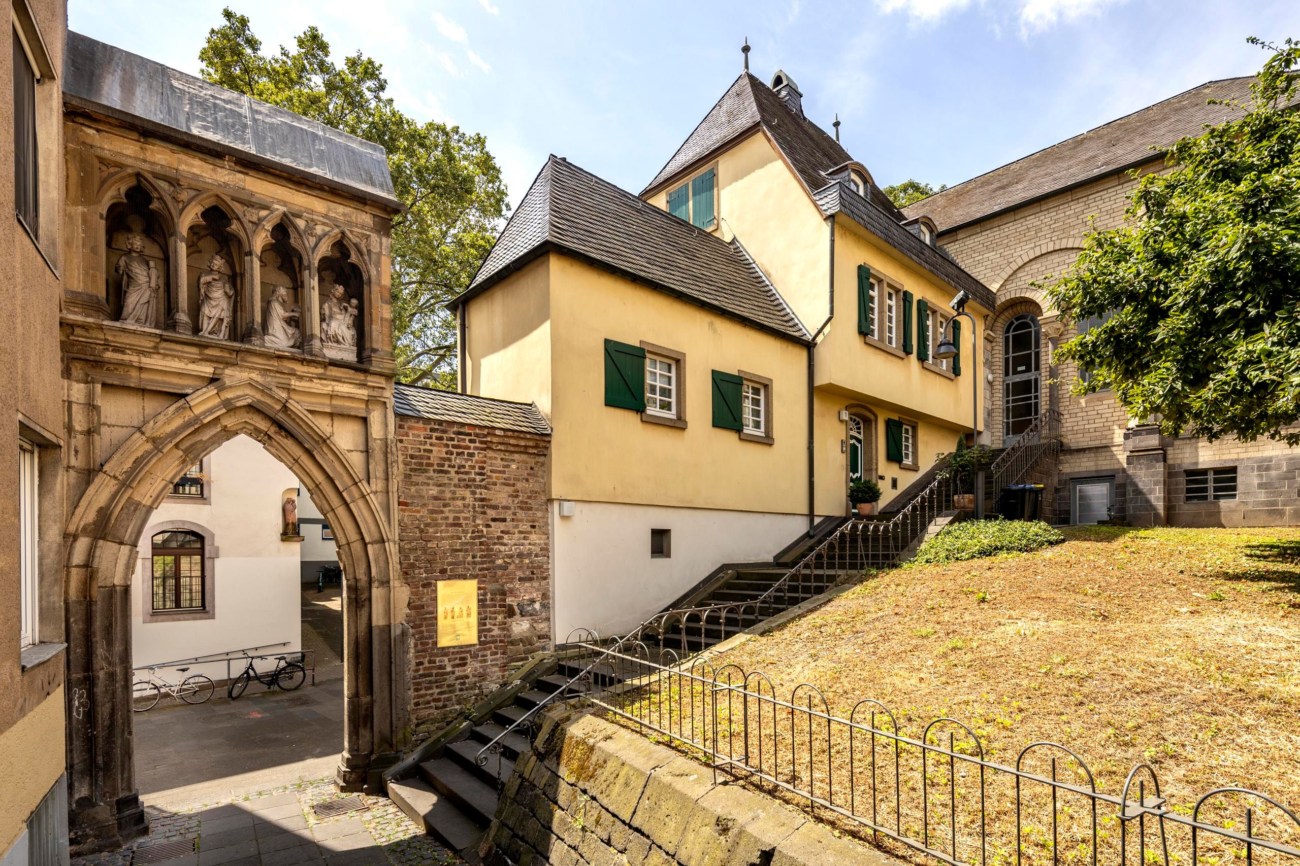 Historische Gebäude und ein Torbogen des Sankt Maria im Kapitol in Köln mit Skulpturen.