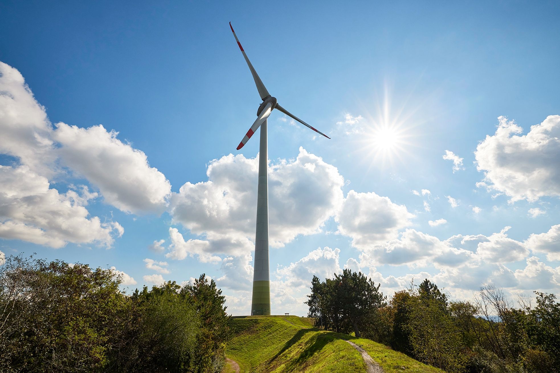 Windrad auf der Halde Hoppenbruch unter blauem Himmel mit Sonne und Wolken.