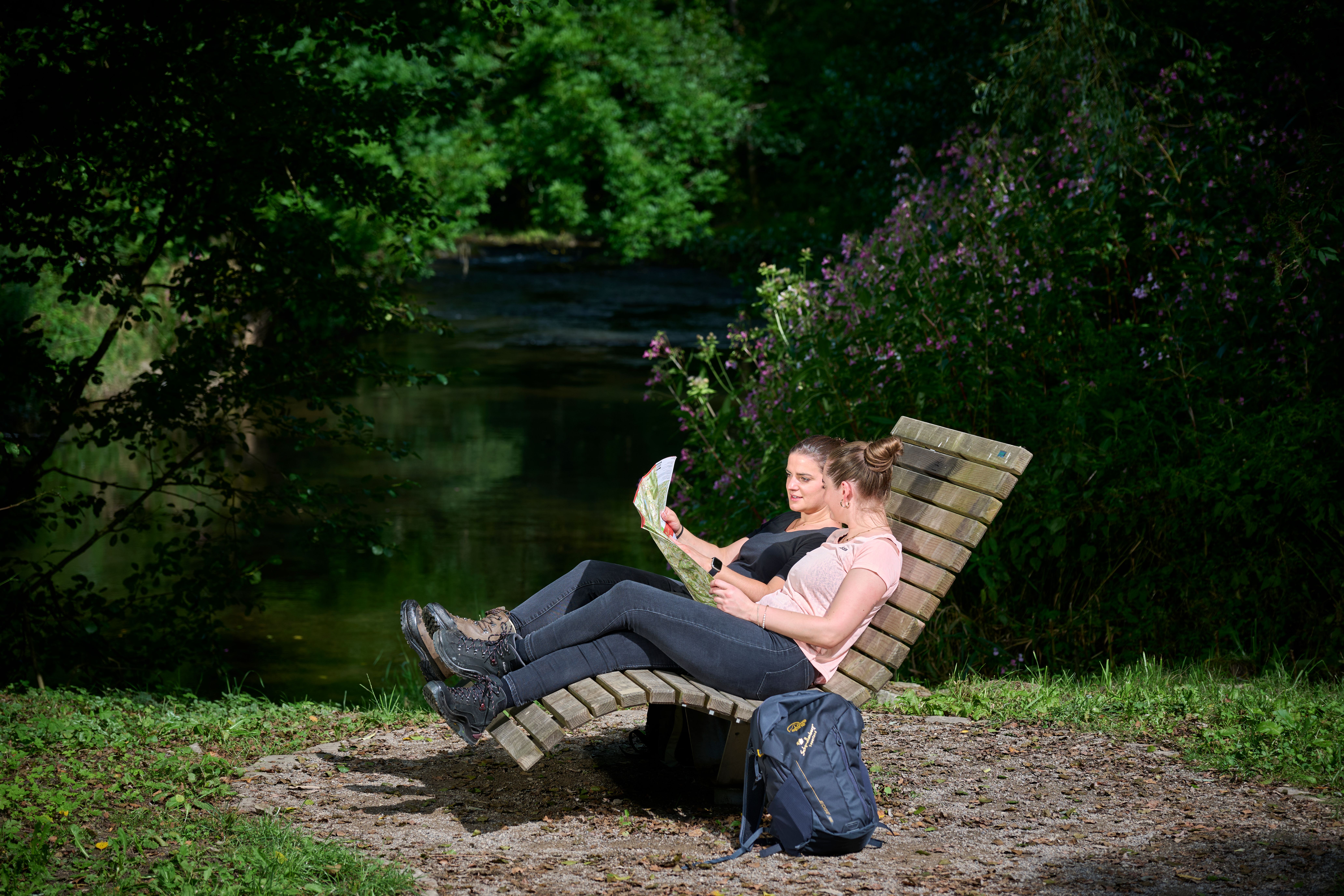 Zwei Personen sitzen auf einer Bank und schauen in eine Wanderkarte.